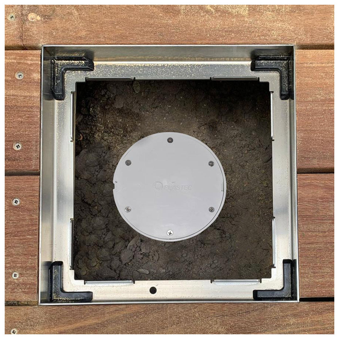 Square HIDE Access Cover frame set into timber decking, lid removed to reveal a round plastic service access cap in the cavity below.