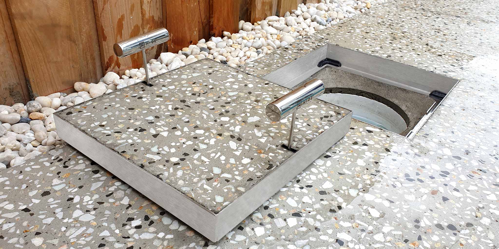 HIDE stainless steel Skimmer Cover lifted open with exposed aggregate concrete inlay, revealing round skimmer box opening