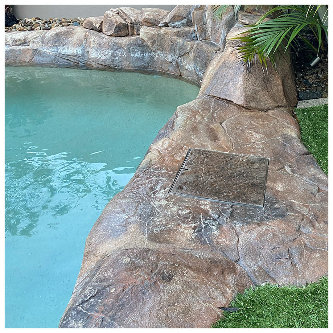 Flush-mounted HIDE Stainless Steel Cover with stone inlay beside a swimming pool in rock coping.