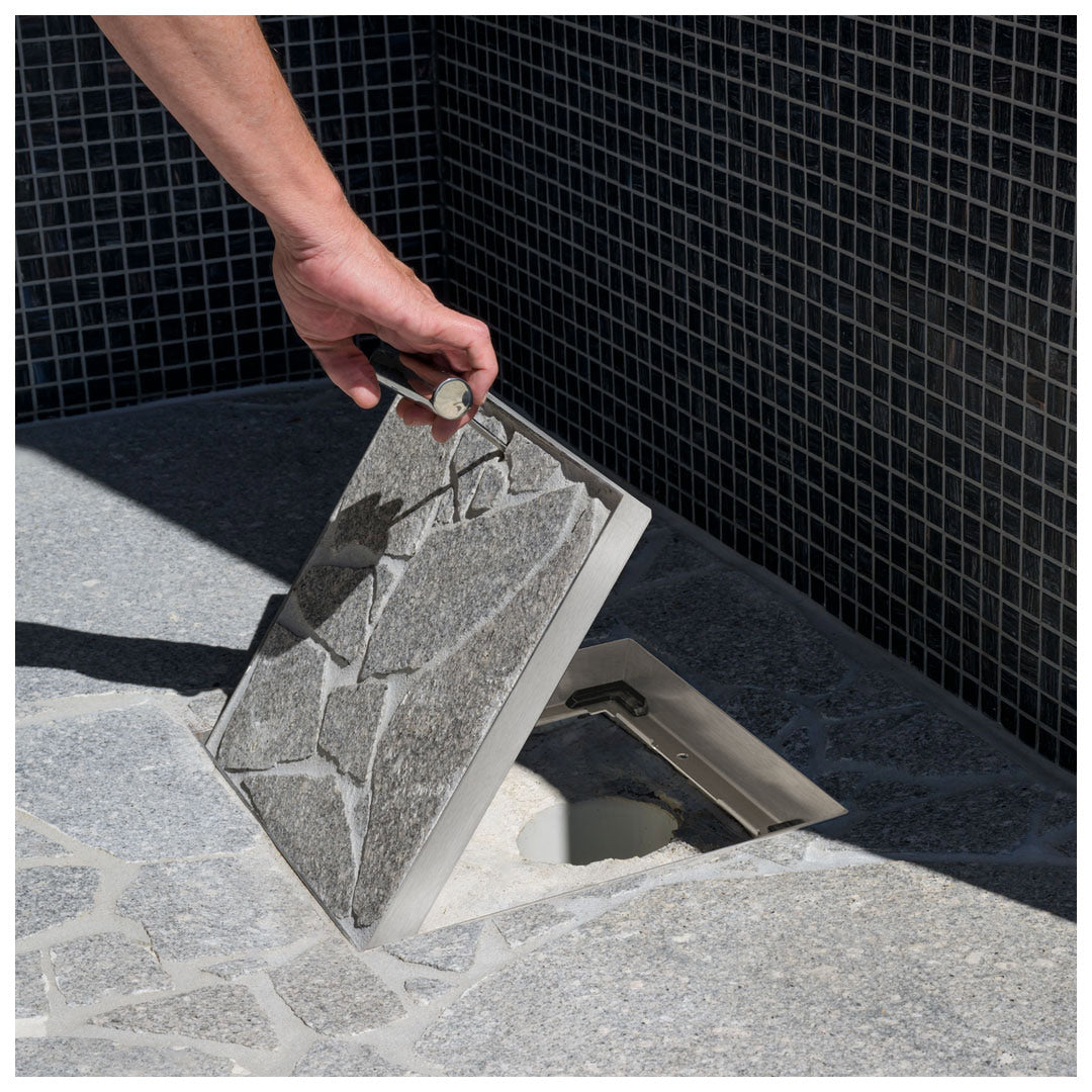 HIDE Drain Cover with grey crazy pave inlay being lifted to see drainage pipe underneath.