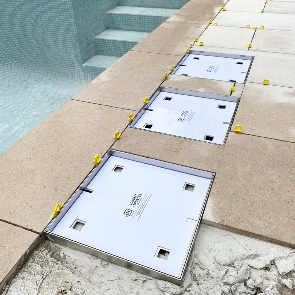 Three HIDE inlay access covers set flush in pool paving with tile spacers for level installation.