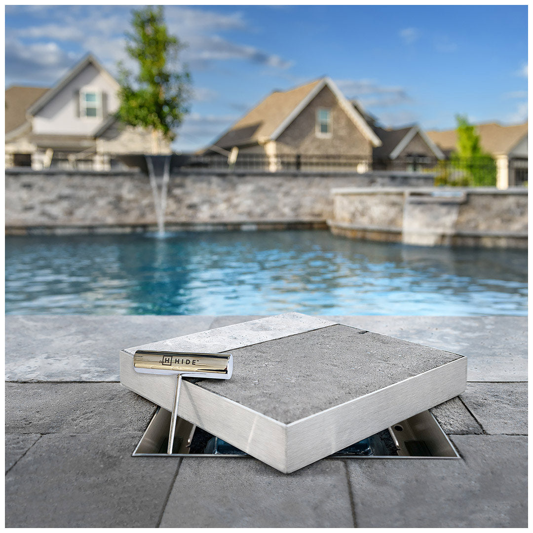HIDE stainless steel inlay skimmer lid lifted open in pool paving, showing concealed skimmer access.
