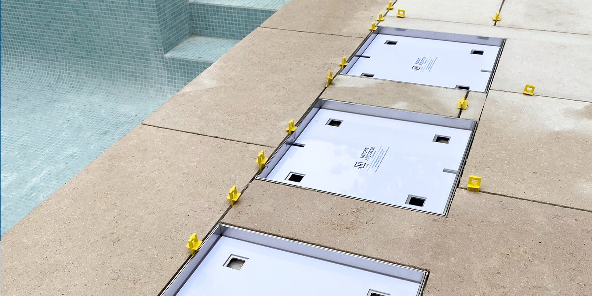 Three flush-mounted HIDE Skimmer Covers installed in poolside pavers, aligned with finished stone levels.