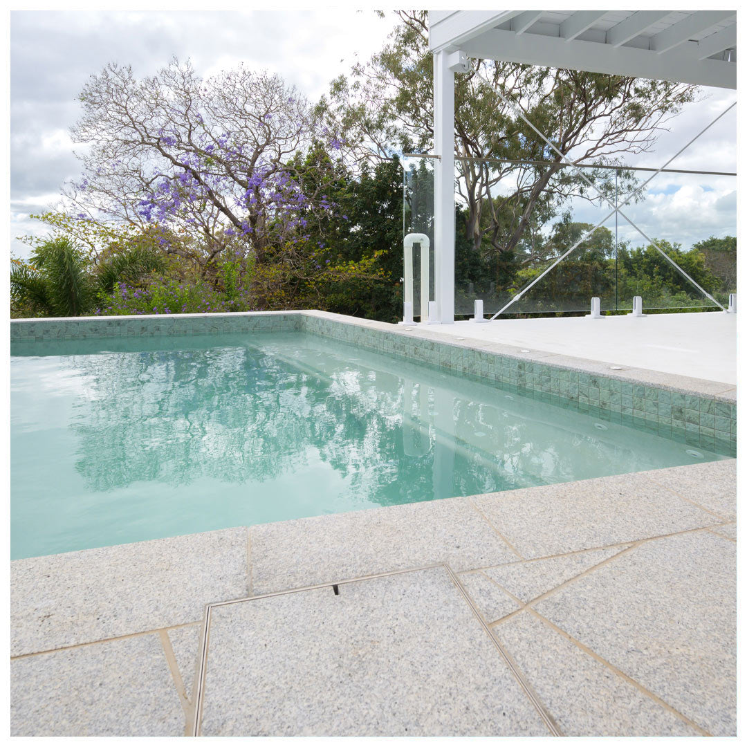 Flush-mounted HIDE Skimmer Cover in light grey stone tile beside a swimming pool.