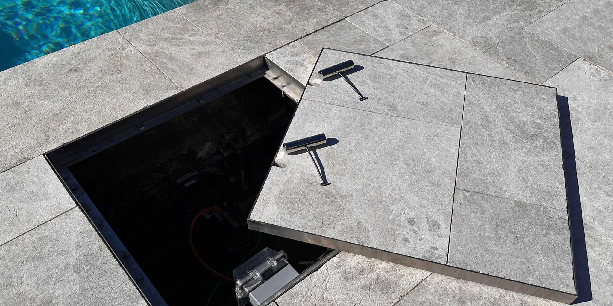 Open HIDE stainless steel manhole access cover with stone inlay, providing service access to a pool swimjet system.
