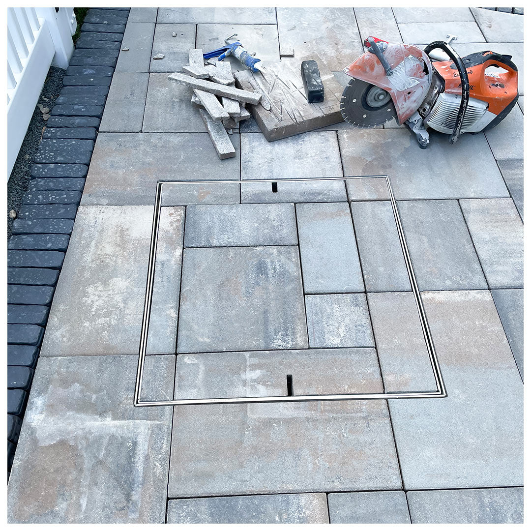 HIDE Manhole Cover with grey paving inlay covering a service access point. Paving pattern has continued through the Cover to create an seamless finish.